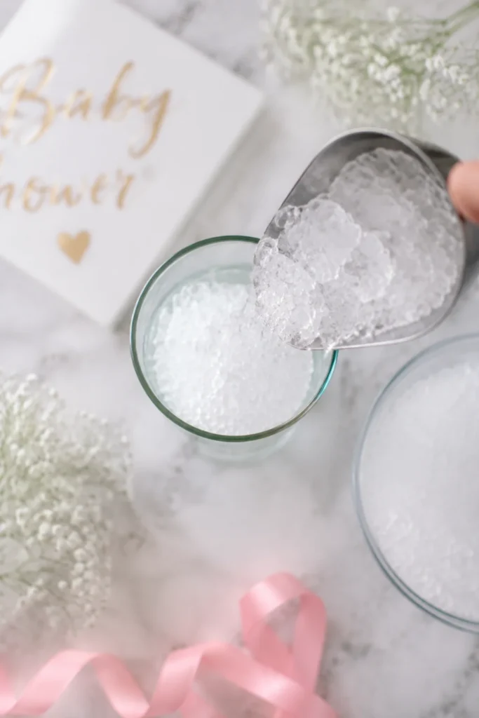 Tall glass being filled with crushed ice, soft pastel baby shower style.