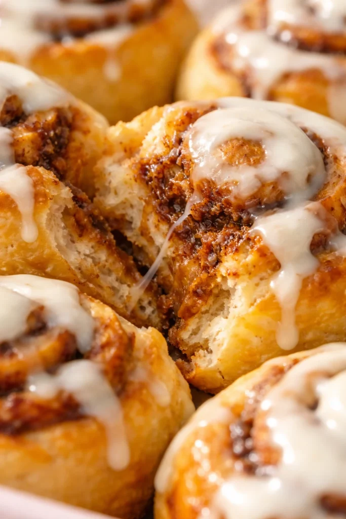 Extreme close-up of a cinnamon roll torn open showing gooey cinnamon filling, buttery layers, and melted icing.