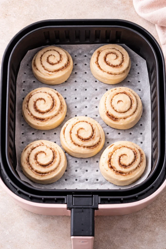 Raw cinnamon rolls spaced evenly inside an air fryer basket before cooking.