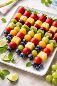 Colorful fruit skewers with strawberries, grapes, pineapple, kiwi, and blueberries arranged on a white platter for a baby shower.