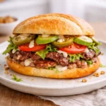 Mexican torta sandwich on a ceramic plate made with bolillo bread, grilled steak, avocado slices, tomato, lettuce, and creamy sauce
