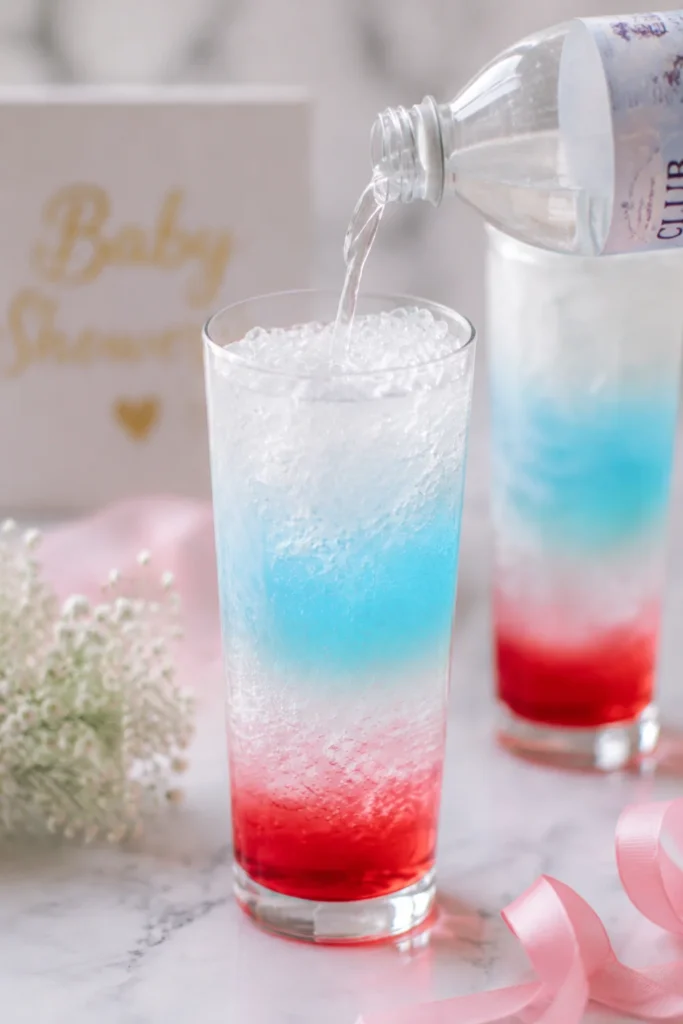 “Gently pouring cream into layered soda, creating swirling effect, pastel baby shower aesthetic.”